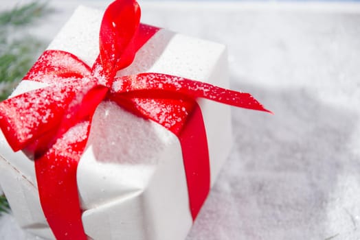 White gift box with a red bow in the snow, close-up