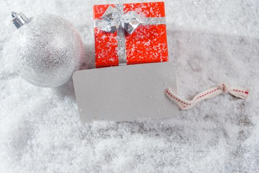 Gift box, white ball and card in the snow, space for text
