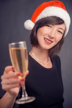 Happy young woman in santa hat is holding glass with champagne