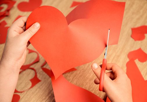 Unrecognizable child cuts a red paper heart