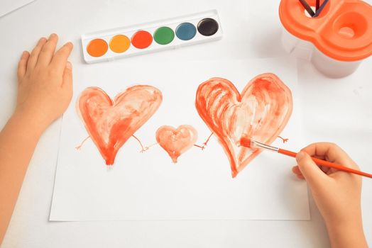 Unrecognizable child paints three red hearts, concept of family