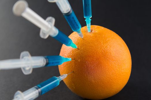 Сhemical liquid in the syringe injected into grapefruit on a black background