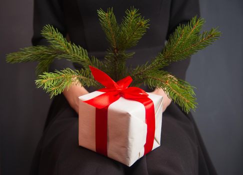 Woman is holding a white gift box and branch fir-tree