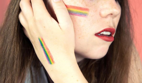 Portrait of a young woman with rainbow Flag on cheek and body, the LGBT community on a colorful pink background freedom, LGBTQ concept beauty