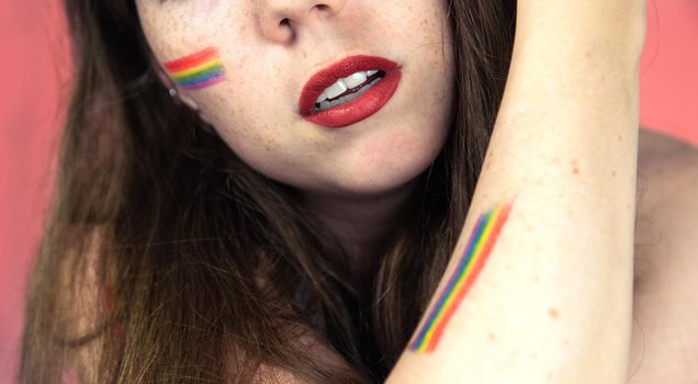 Portrait of a young woman with rainbow Flag on cheek and body, the LGBT community on a colorful pink background freedom, LGBTQ concept beauty