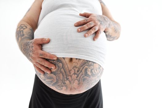 Happy fat man with big belly and tattoes in sports wear is holding his stomach