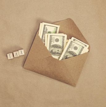 Personal tax income concept, cube wooden block with word TAX with envelope with dollars, business and financial concept copy space top view craft paper