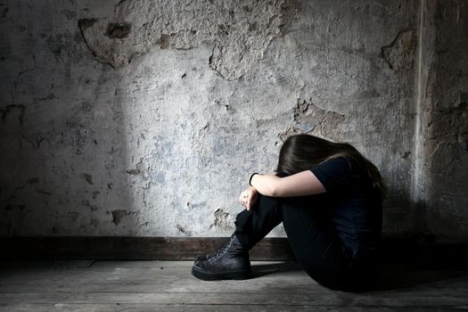 Depressed and lonely girl sitting alone in a spooky abandoned dirty old room on the wooden floor feeling miserable and anxiety cry over her life, depression and addiction issues concept with copy space shadows and dark place