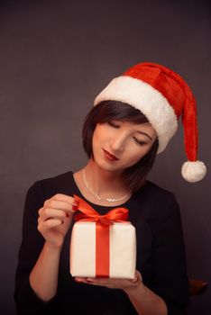 Woman in santa hat is opening a white gift box with red bow