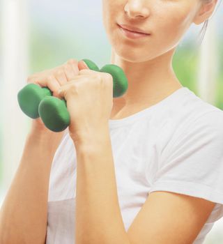 Young woman is doing exercises with dumbbells in a gym