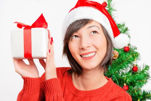 Young woman holds a present and looks dreamy up on the background of Christmas tree