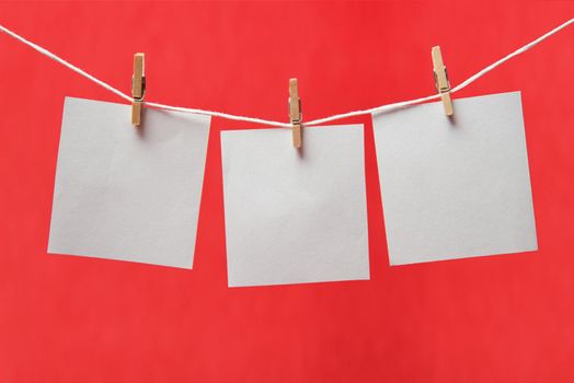 Sheets of paper on a clothespins on a red background, space for text