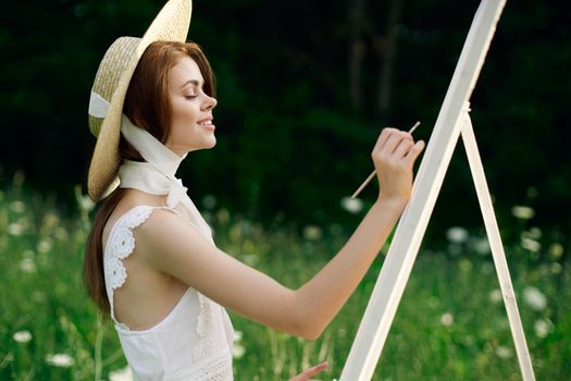 Woman in white dress paints a picture on nature easel. High quality photo