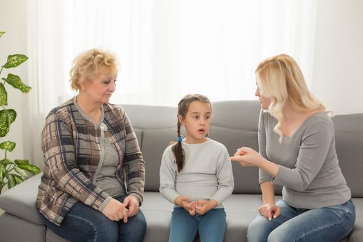 Frustrated girl sitting at home while mother and grandmother berating her