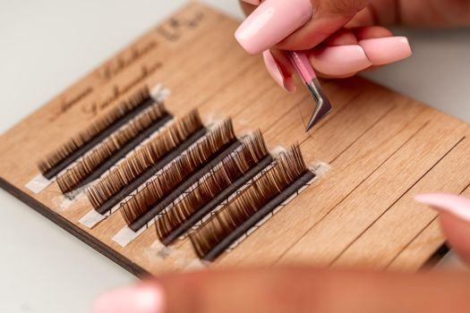 Eyelash extensions, lashmaker tools. Artificial eyelashes on a white tablet and pink silicone brush comb, close up