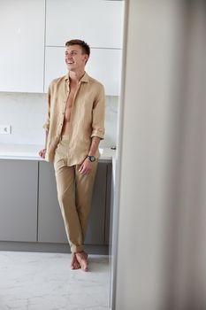 Happy handsome man is standing on minimalistic kitchen and smiling