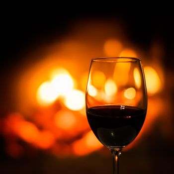 A wineglass of red wine on the background of the fireplace lights. Christmas holiday concept