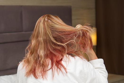 a blonde with dyed hair combing her tangled hair after a shower with a wooden comb. close-up