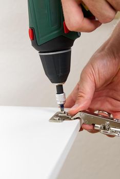 the carpenter screws the hinge on the furniture door. DIY Furniture assembly service concept