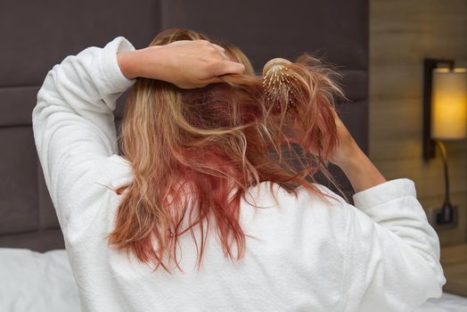 a blonde with dyed hair combing her tangled hair after a shower with a wooden comb. close-up