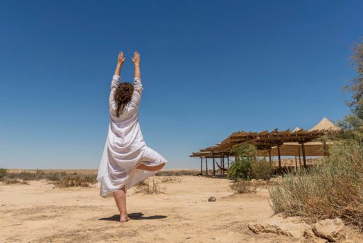 A woman stands in the desert and looks at the horizon. White clothing fluttering in the wind. Concept for relaxation, inner looking, meditation, peace of mind. High quality photo