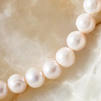 Nature white string of pearls on marble background in soft focus, with highlights.