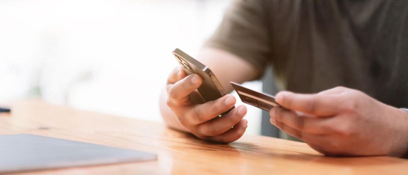 Online payment, Man's hands holding a credit card and using smart phone for online shopping at coffee cafe shop.