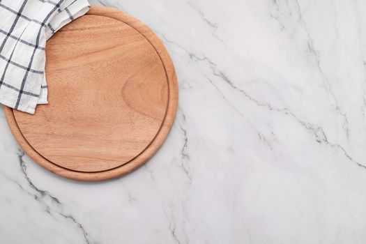 Empty wooden pizza platter with napkin  set up on marble stone kitchen table. Pizza board and tablecloth on white marble background.