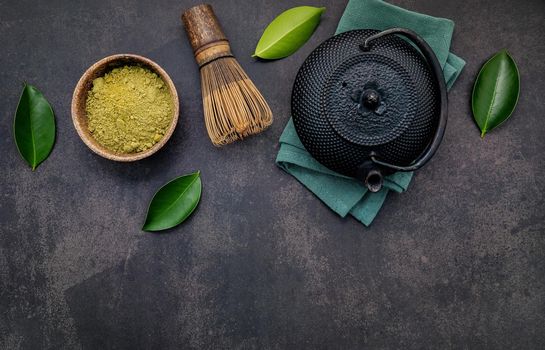 Black cast iron tea pot with herbal tea set up on dark stone background.