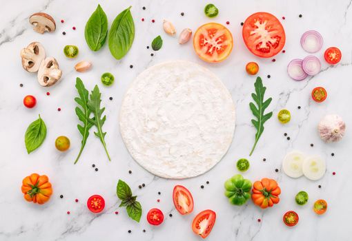 The ingredients for homemade pizza set up on white marble background.