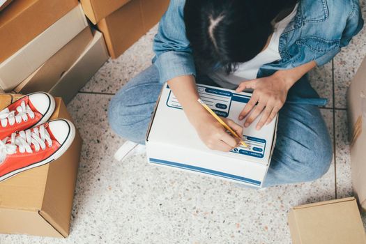 Closeup hand of young woman writing address on parcel box for delivery order to customer, shipping and logistic, merchant online and seller, business owner or sme, online shopping.
