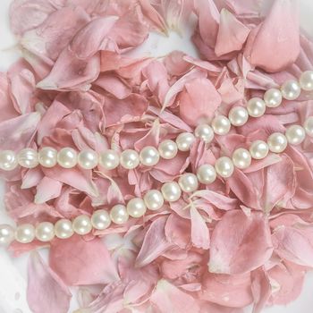 Beautiful pearl necklace on a background of pink rose petals. Ideal for greeting cards for wedding, birthday, Valentine's Day, Mother's Day.