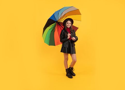 happy teen girl in hat and leather clothes under rainbow umbrella, autumn rain.