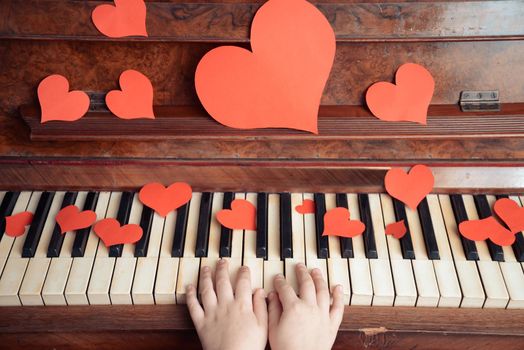 Child is playing on a piano on Valentine's Day, side view, face is not visible