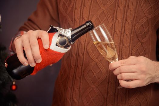 Unrecognizable man in sweater is pouring champagne into a glass