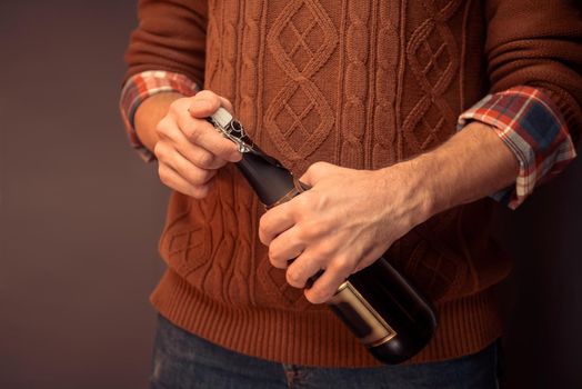 Unrecognizable man in sweater is opening champagne, close-up