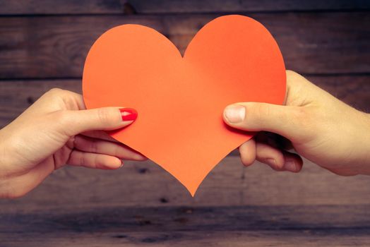 Male and female hands hold red paper heart, concept of love