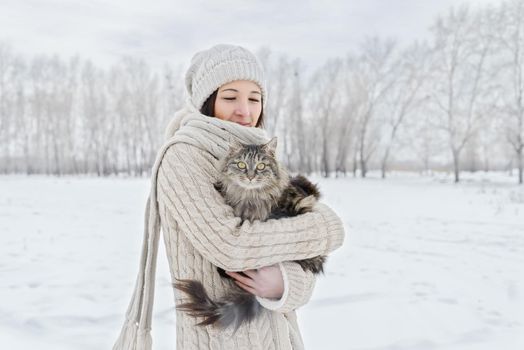Young beautiful woman is hugging cat outdoors in winter