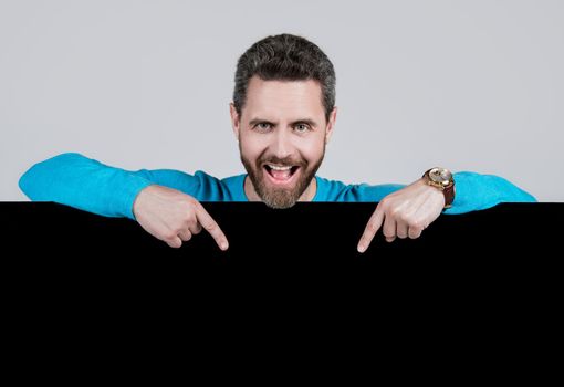 happy bearded man pointing finger on blank black paper banner with copy space for creativity, announcement.