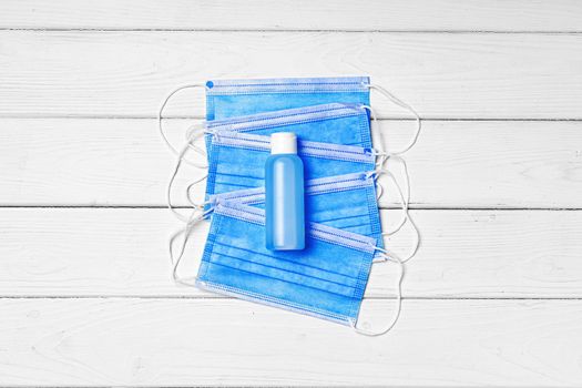 Medical face mask and sanitizer gel on white wooden background close up