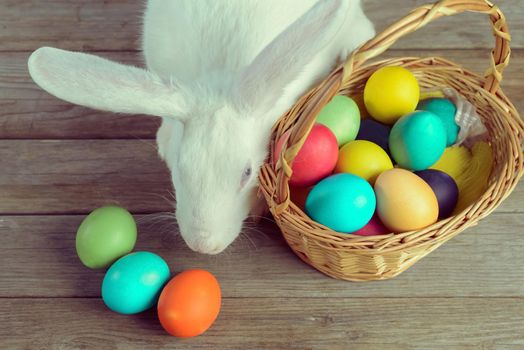 White Easter bunny with basket of colored eggs on wooden table, top view