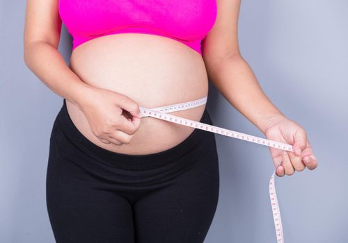 close-up belly of Pregnant woman with measuring tape on gray wall background