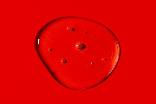 Clear transparent liquid gel drop or smear isolated on vivid red background. Top view. Virus protection or cosmetics concept. Serum texture