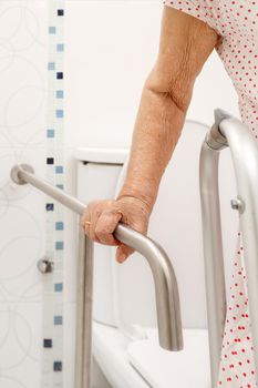 Elderly woman holding on handrail in toilet.