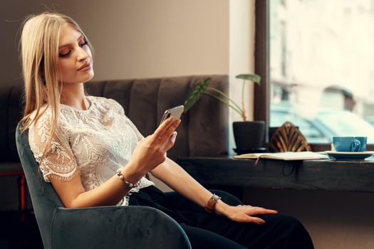 Happy young woman using her smartphone while sitting in cafeteria. Close up.