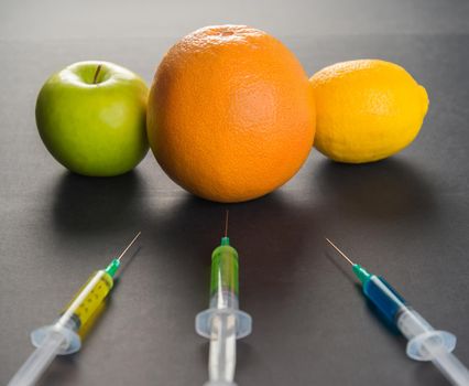 Сhemical liquid in the syringe and fruits on a black background