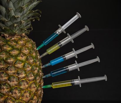Chemical liquid in the syringe injected into pineapple on a black background