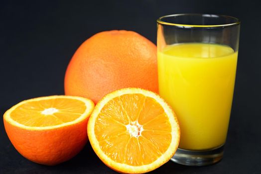 Citrus fruits and glass of juice on a black table