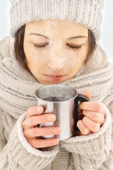 Young woman in a scarf and cap holds a cup of hot coffee outdoor