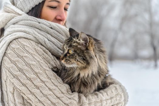 Young woman holds fluffy cat in winter, close-up